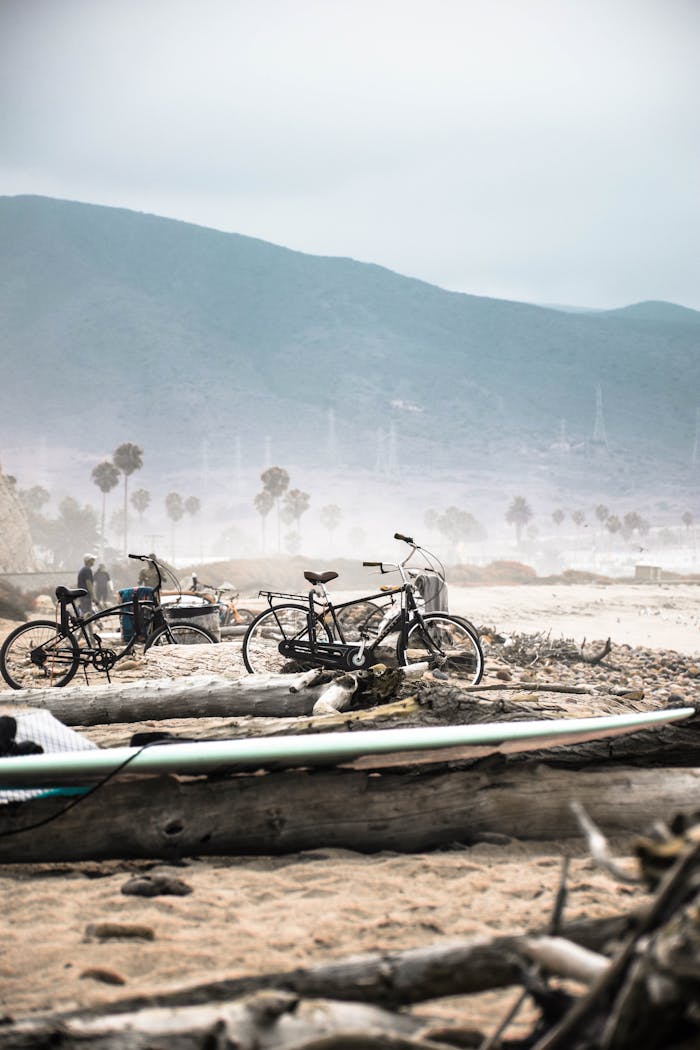 Bicycles resting on a sandy beach with majestic mountains in the background and mist in the air.